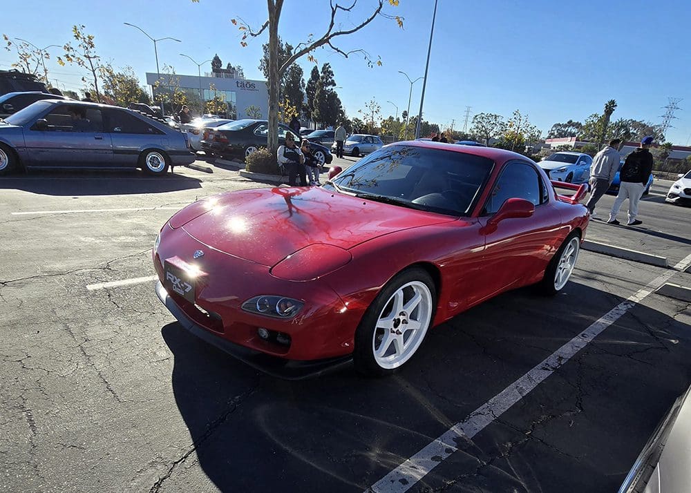 Red sports car parked in a sunny lot with white rims.