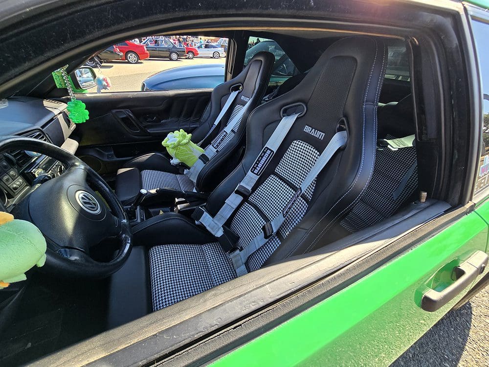 Interior of a green car with black racing seats and harnesses.