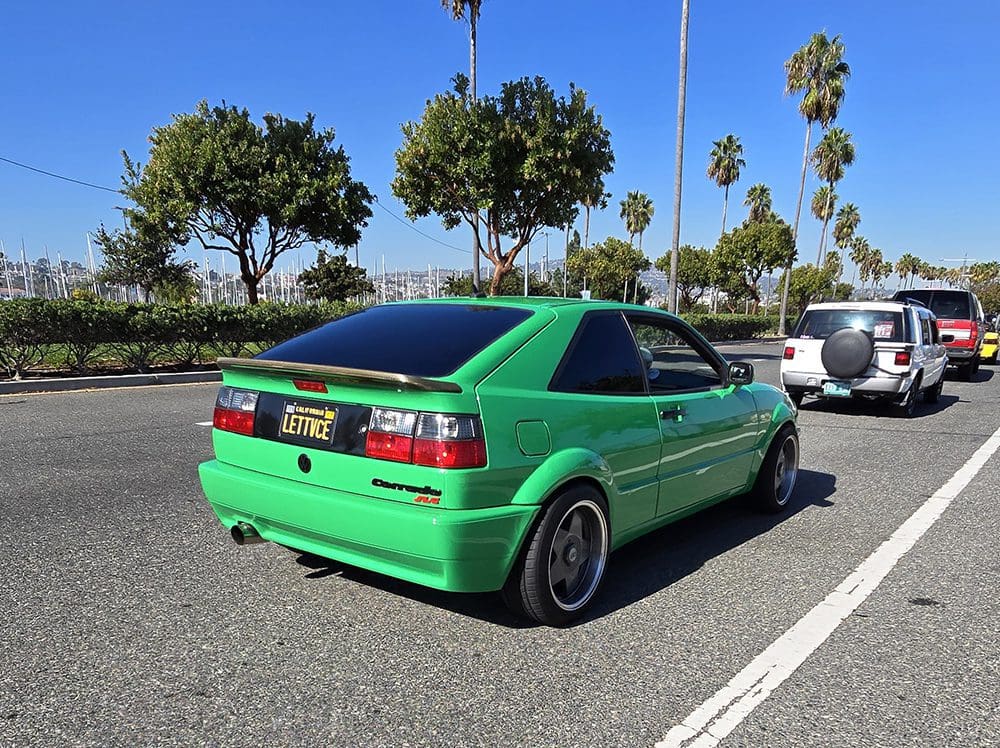 Green sports car parked in a sunny lot with palm trees.