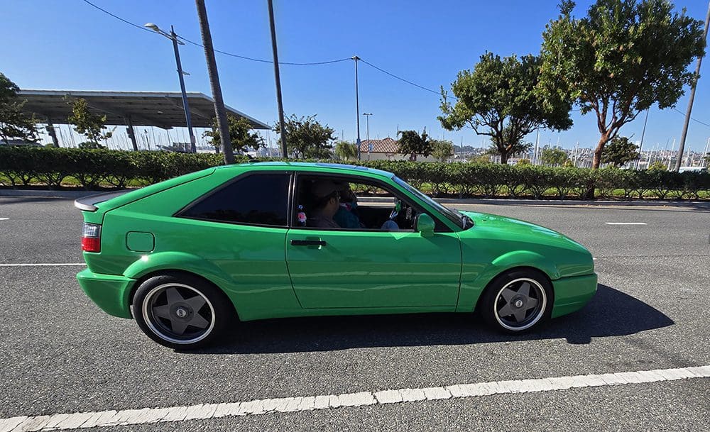 Green vintage sports coupe parked on the street with a clear blue sky.