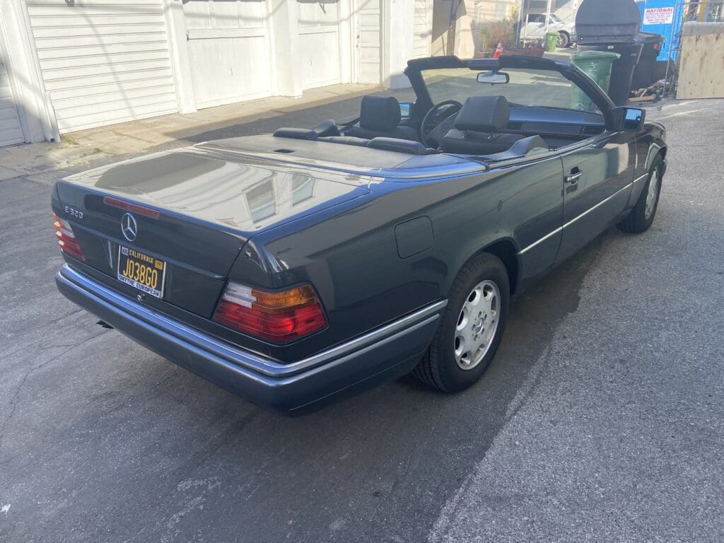 Classic blue convertible car parked on a street in sunlight.