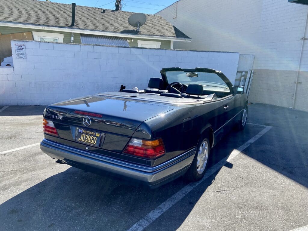 Classic black convertible car parked in a driveway on a sunny day.