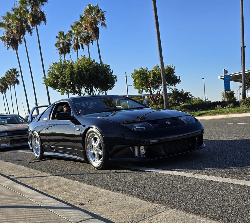 A sleek black sports car parked on a sunny street with palm trees.