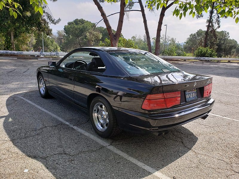 Classic black sedan parked on a sunny street with trees.