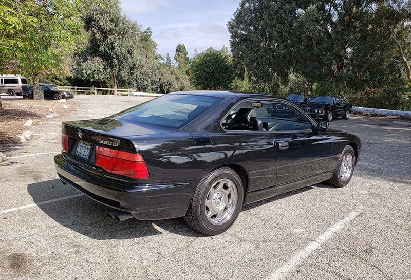Black sports coupe parked in a sunny lot with trees.