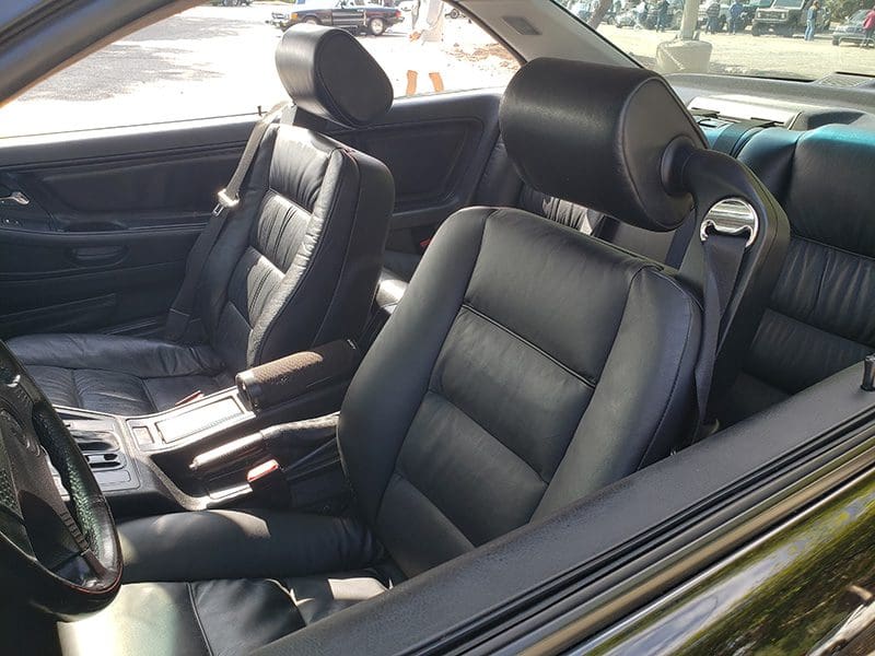 Black leather car seats with headrests and armrest in a sunny environment.