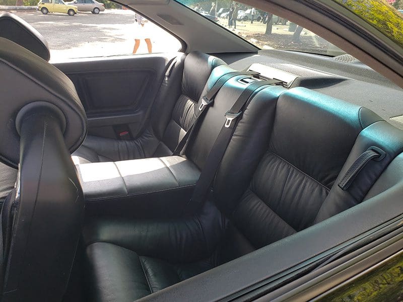 Interior view of a car showing black leather rear seats with seat belts.