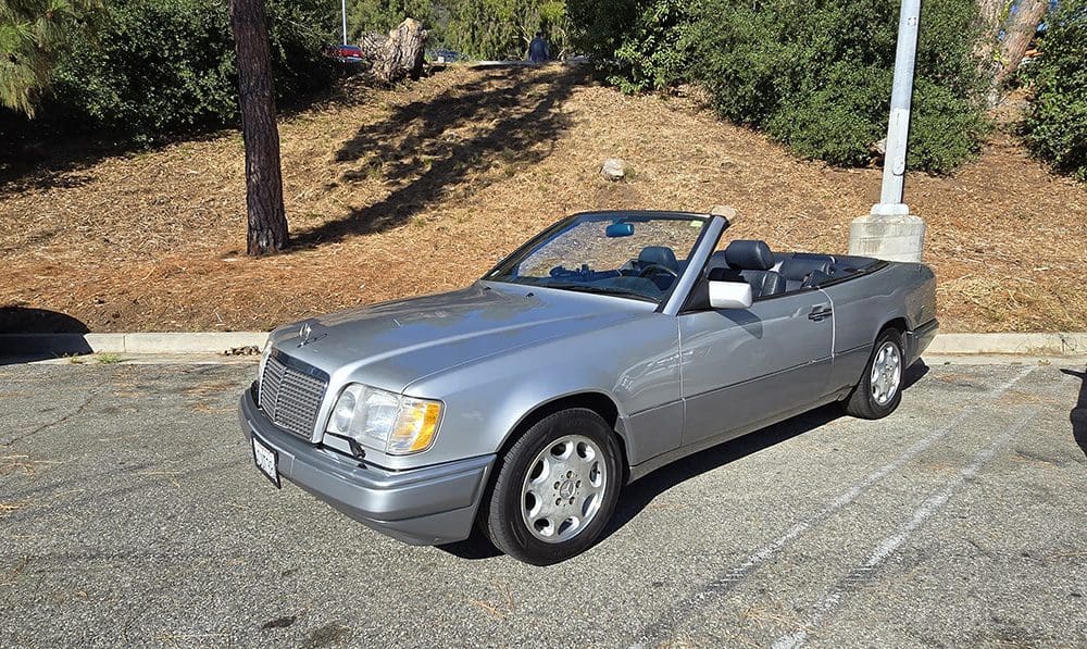 Silver convertible car parked on a sunny roadside.