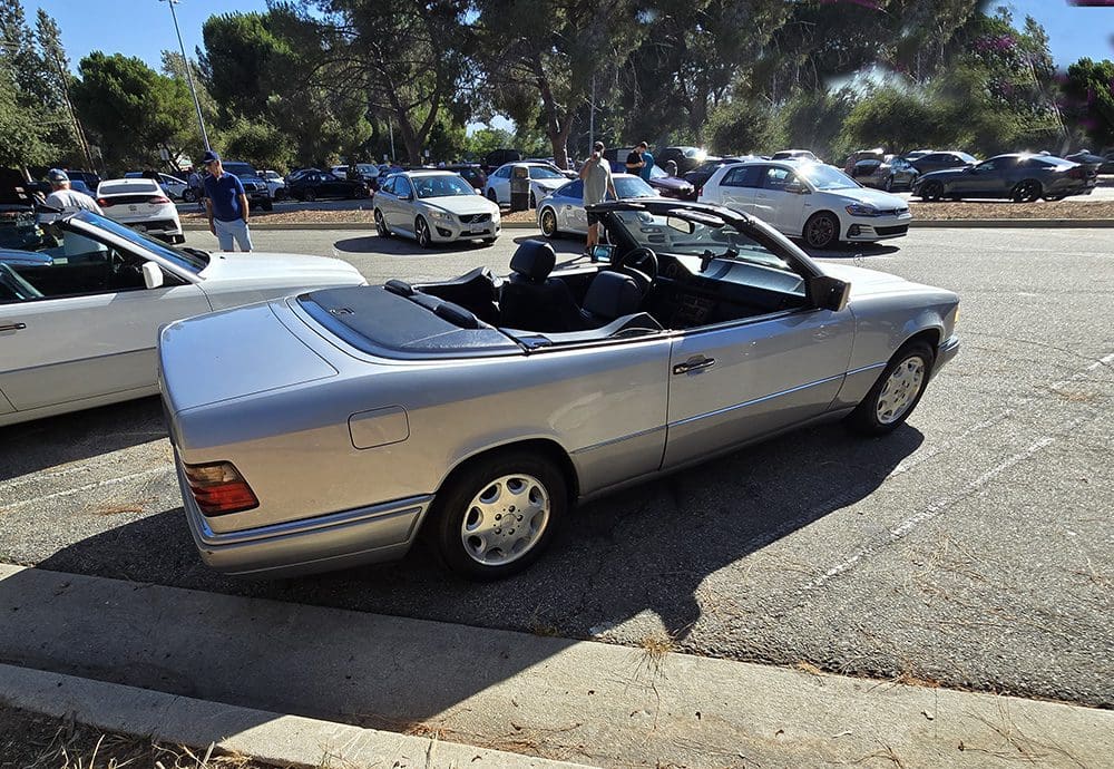 Silver convertible car parked on a sunny roadside.