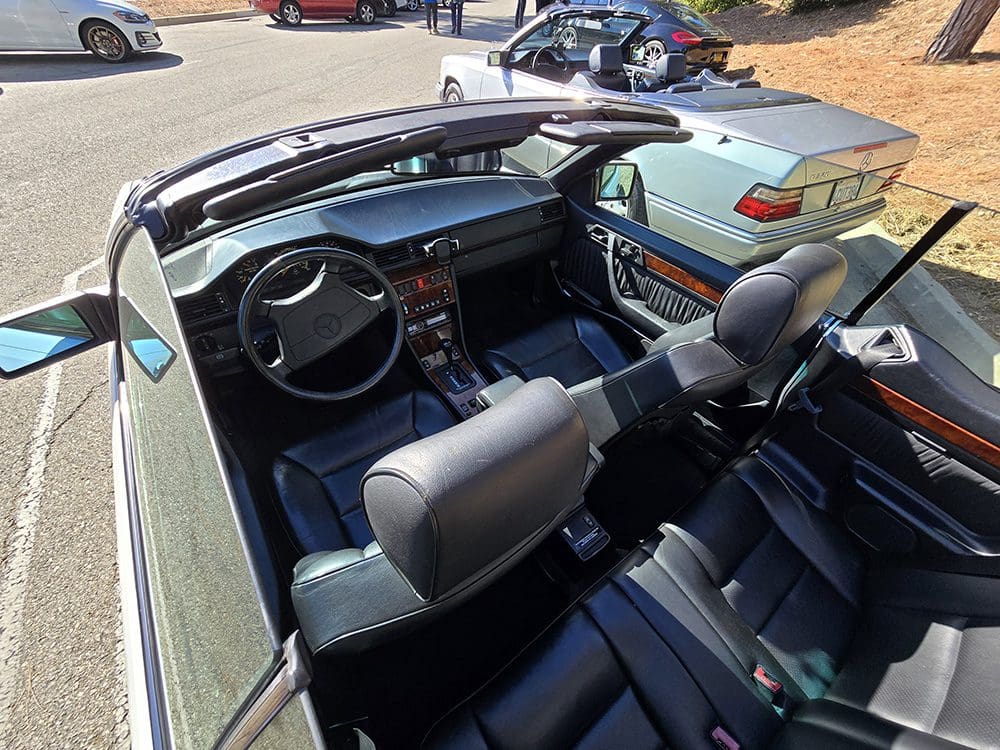 Interior of a convertible car with black leather seats and a wooden dashboard.