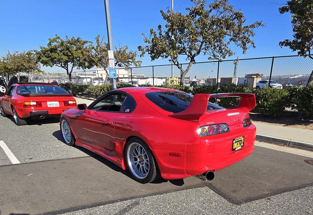 Red sports car with custom rims parked outdoors under trees.