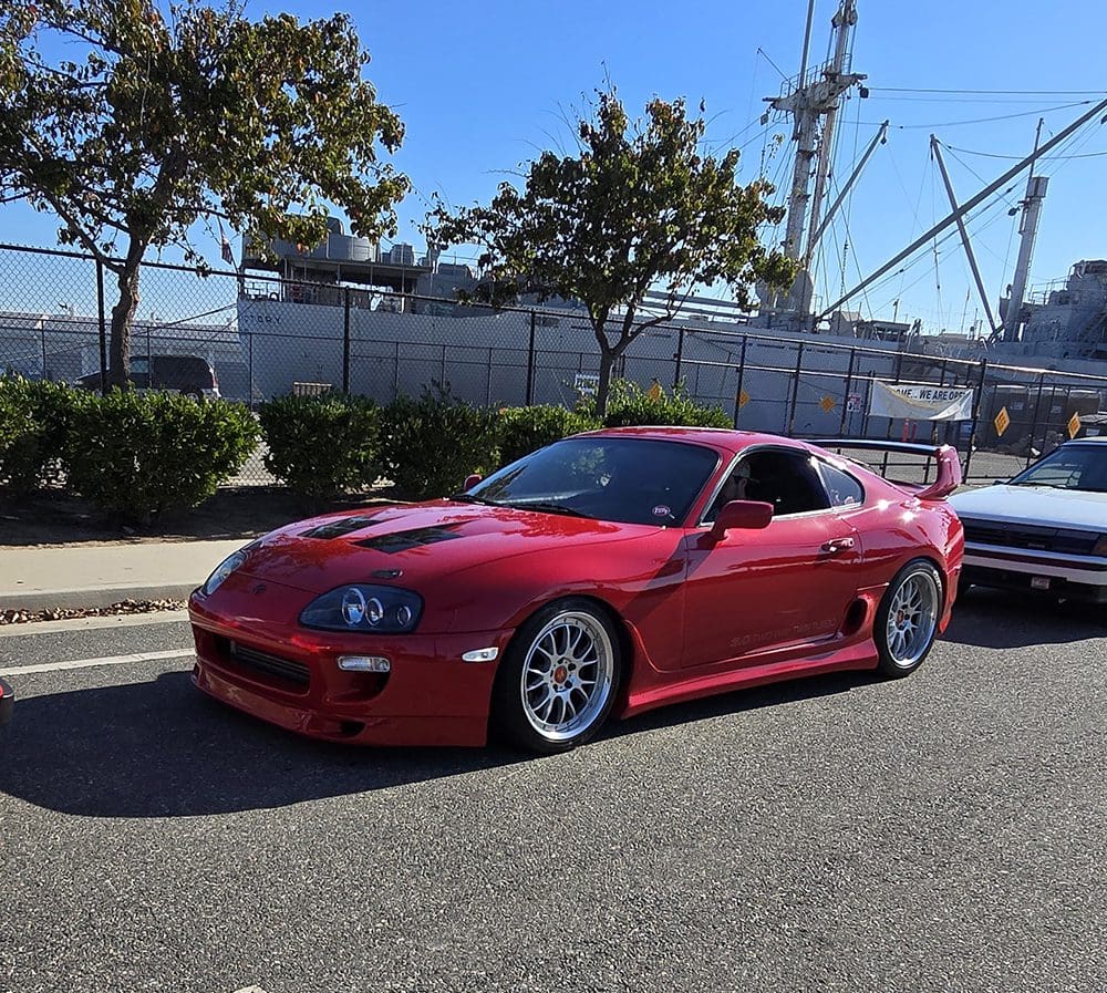 Red sports car parked on a street near trees and construction cranes.