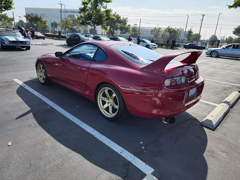 Red sports car with a large rear spoiler parked in a lot.