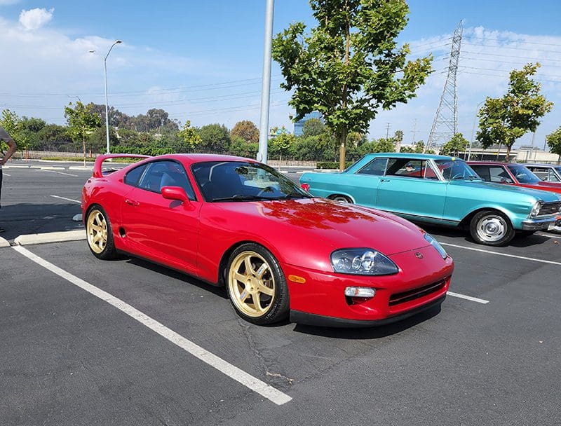 Red sports car with gold wheels parked outdoors on a sunny day.