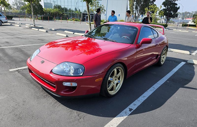 Red Toyota Supra parked on a sunny day with gold wheels.