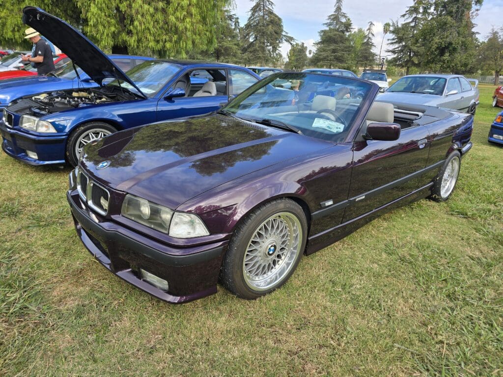 Classic purple BMW convertible parked at a car show on grass.
