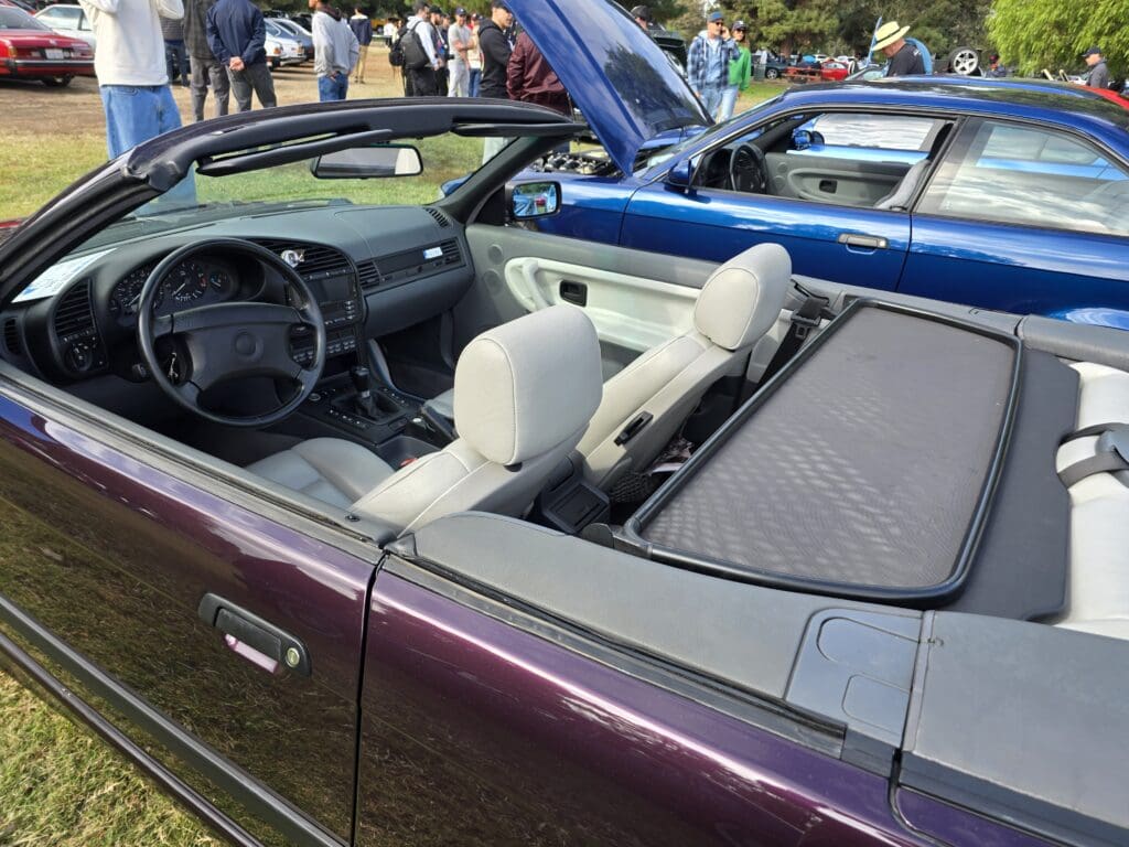 Convertible car with gray interior seats and open roof at a car show.