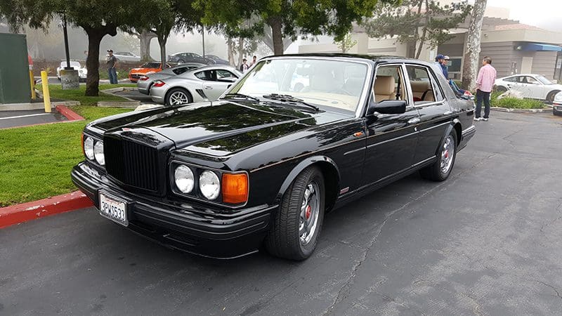 Classic black luxury sedan parked outdoors with trees in the background.
