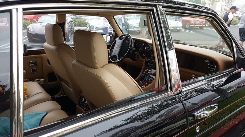 Interior view of a classic car showing beige seats and a wooden dashboard.