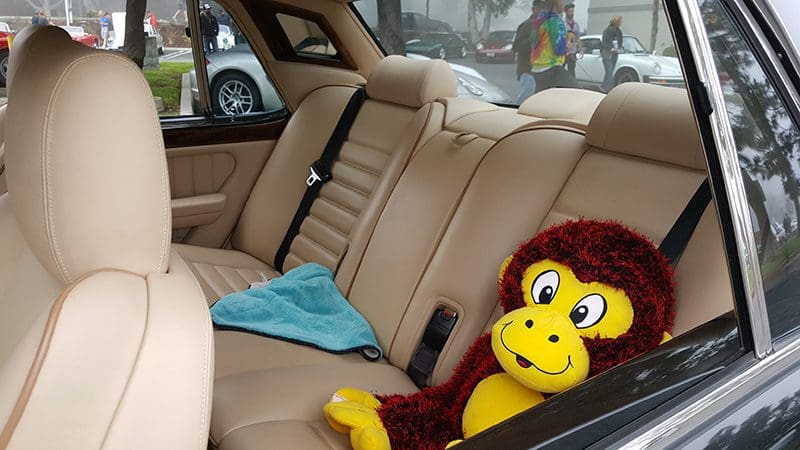 Stuffed monkey toy on a beige car backseat with a blue cloth.