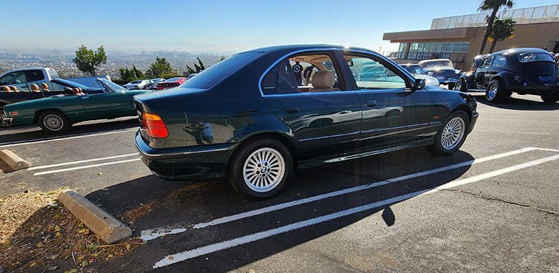 A dark green sedan parked in a parking lot with a scenic background.