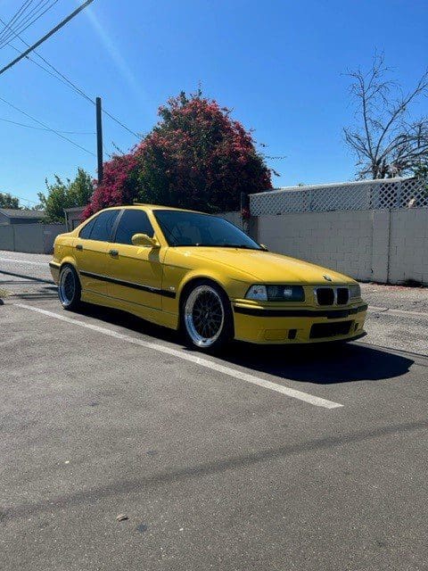 Yellow BMW parked in an empty lot under clear blue sky.