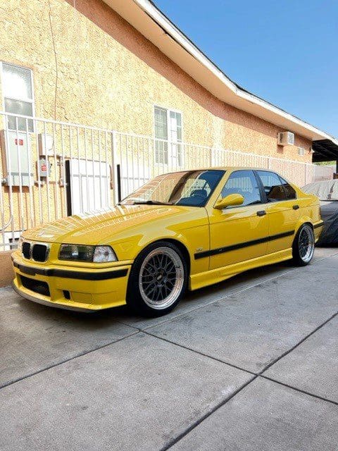 Yellow BMW E36 coupe parked on driveway beside house.