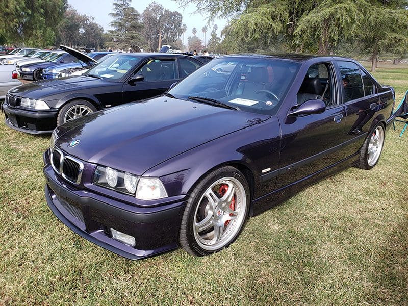 Purple BMW sedan parked on grass beside another car.