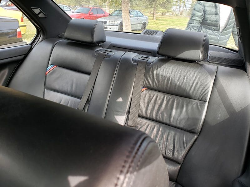 Interior view of a car's leather back seats with headrests and seatbelts.