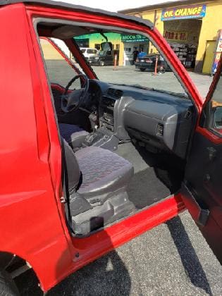 Interior view of a red vehicle with the driver&rsquo;s door open.