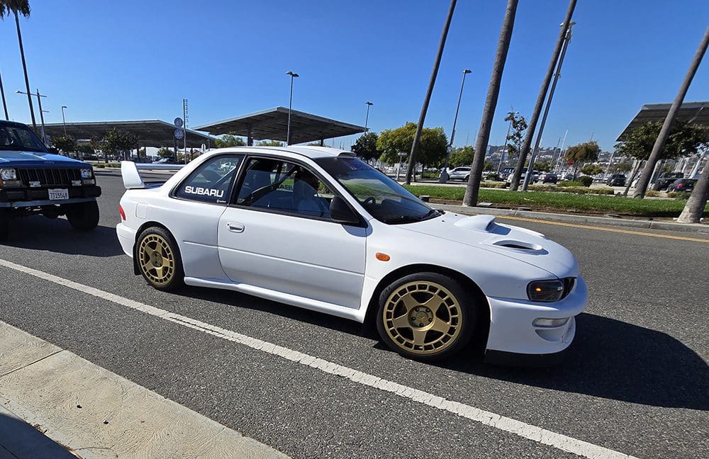 White sports car with gold rims parked outdoors under clear sky.