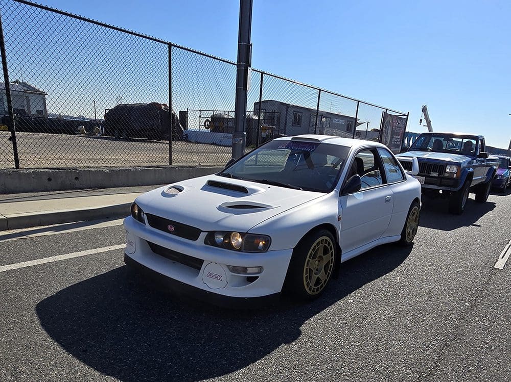 White sports car parked near a fenced area on a sunny day.
