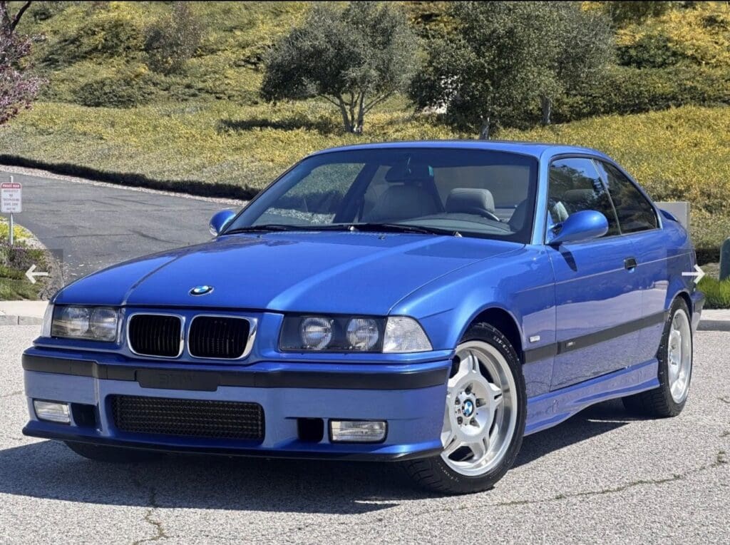 Blue BMW parked on a scenic road with greenery.