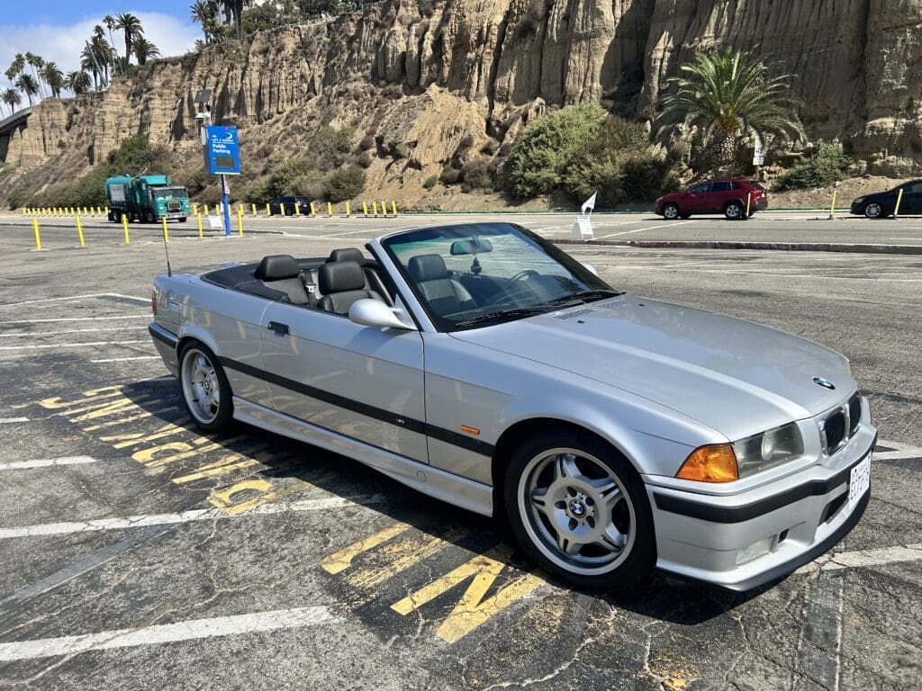 Classic white convertible BMW parked by rocky cliffs on a sunny day.