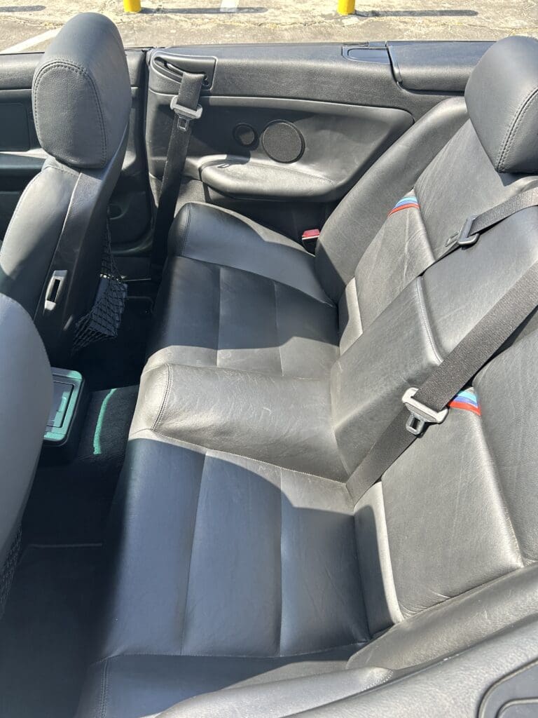 Clean black car backseat with leather seats and seat belts.