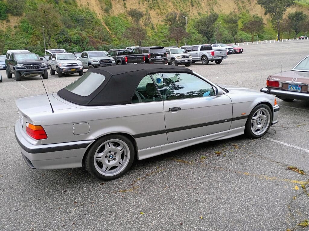 Silver convertible car parked on a roadside with a black soft top.