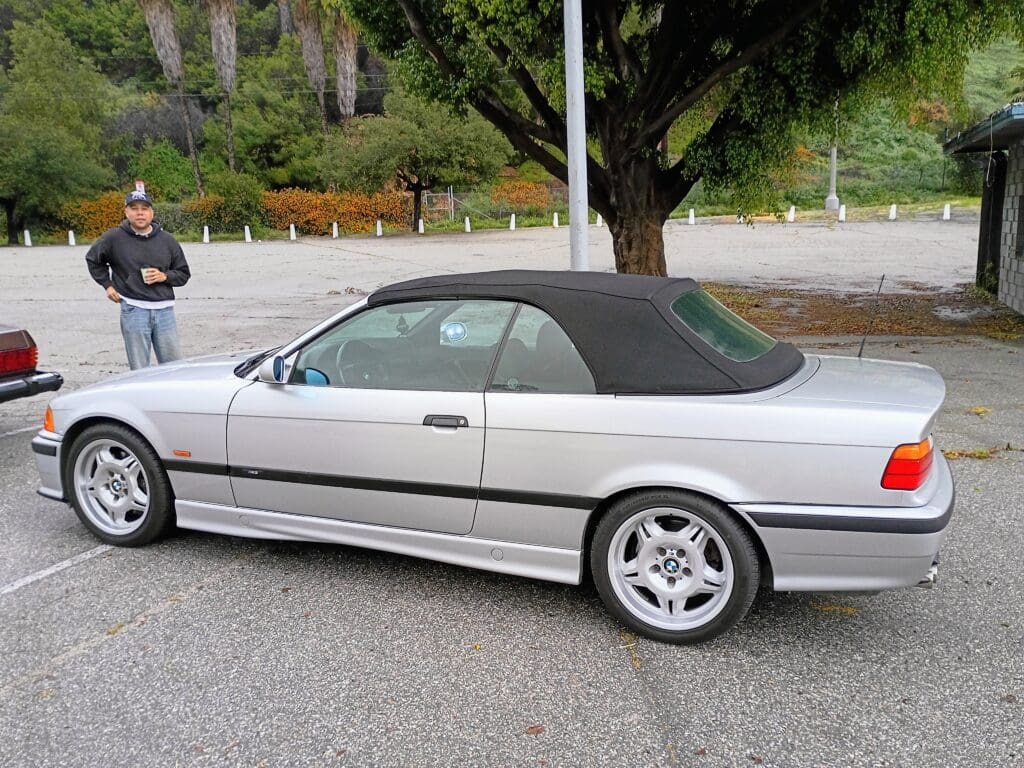 Silver convertible car parked by the roadside with a black soft top.