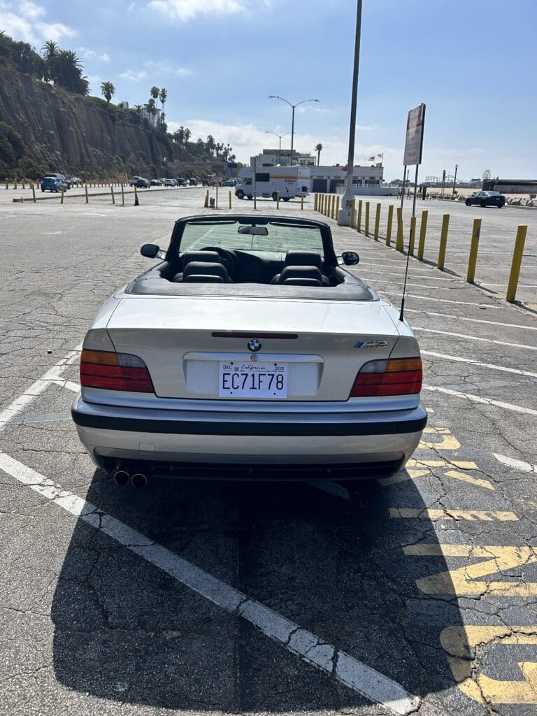 Classic white BMW convertible parked in an empty lot on a sunny day.
